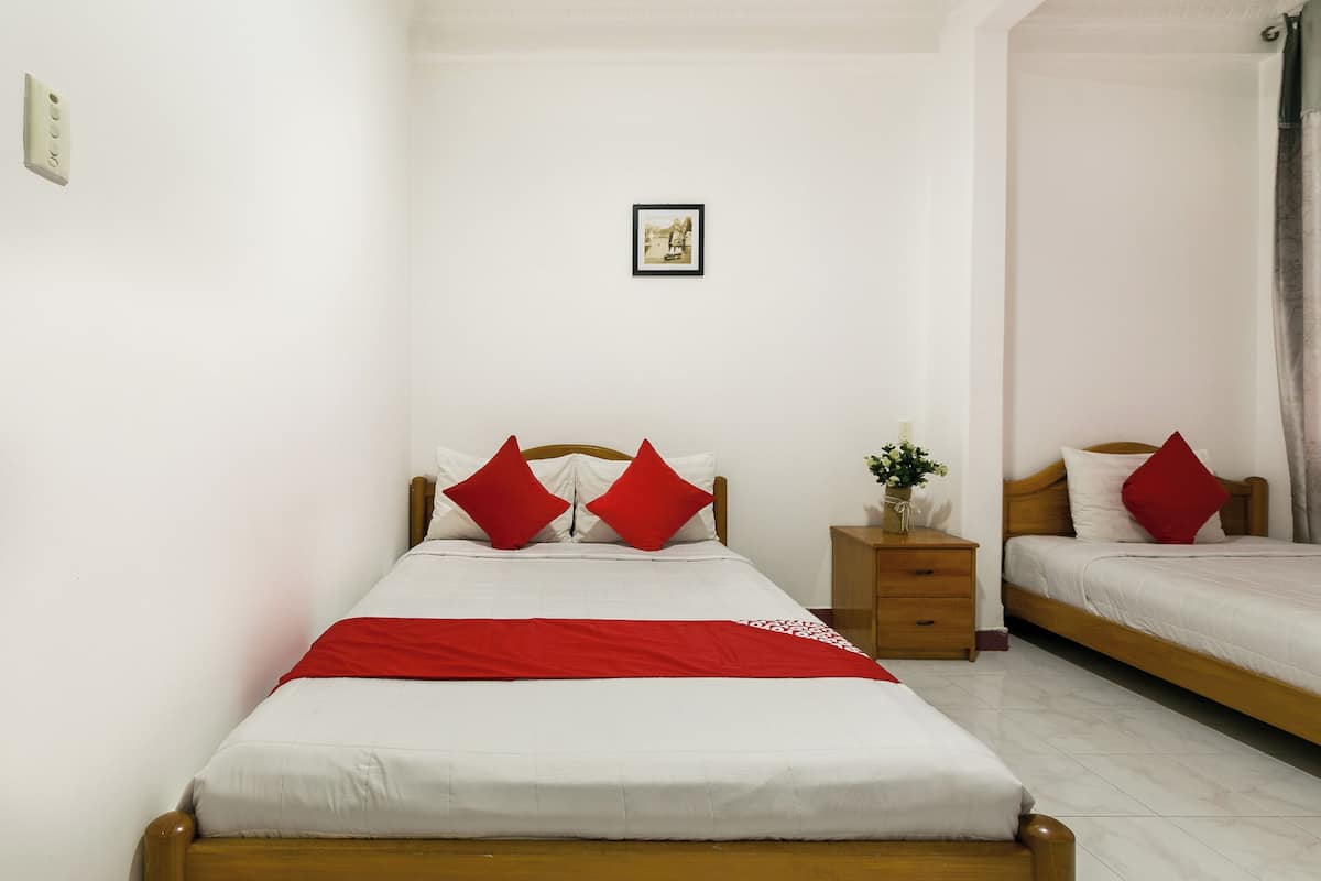 A bedroom with two beds, each with red pillows and a white bedspread. There is a small wooden nightstand with a vase of flowers.
