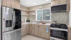 Uma cozinha moderna com geladeira de aço inoxidável, fogão a gás, armários de madeira, uma janela e painel de azulejos.