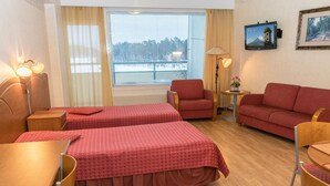 Une chambre d’hôtel avec deux lits simples, un canapé, une chaise, une petite table et un téléviseur fixé au mur.