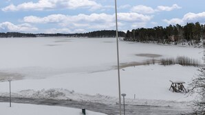 Un paysage enneigé avec un lac gelé, une structure en bois et une forêt en arrière-plan.
