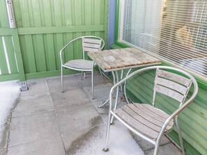 A patio area with a wooden table and metal chairs, a green fence, and a window with blinds. - Hotelli terme, rantahuone 18 by Interhome (Ikaalinen)
