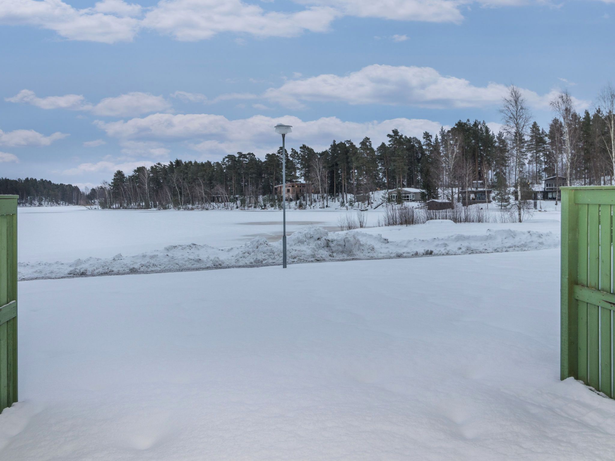 Lumipeitteinen maisema, kirkas taivas, katuvalaisin ja taustalla näkyvä rakennus.