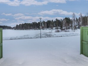 Schneebedeckte Landschaft mit blauem Himmel, einer Straßenlaterne und einem Gebäude im Hintergrund.