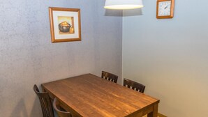 A dining area with a wooden table and chairs, a framed picture on the wall, a floor lamp, and a wall clock.