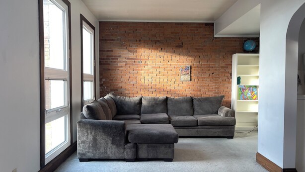 A living room with a sectional sofa, a brick wall, and a white shelving unit. - Loft w/Amazing Deck in Historic Downtown Laramie (Laramie)