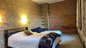 A bedroom with a bed, a brick wall, and a floral wallpaper. - Loft w/Amazing Deck in Historic Downtown Laramie (Laramie)