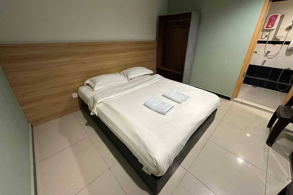 Una cama bien hecha con sábanas y toallas blancas, cabecera de madera y suelo de baldosas.