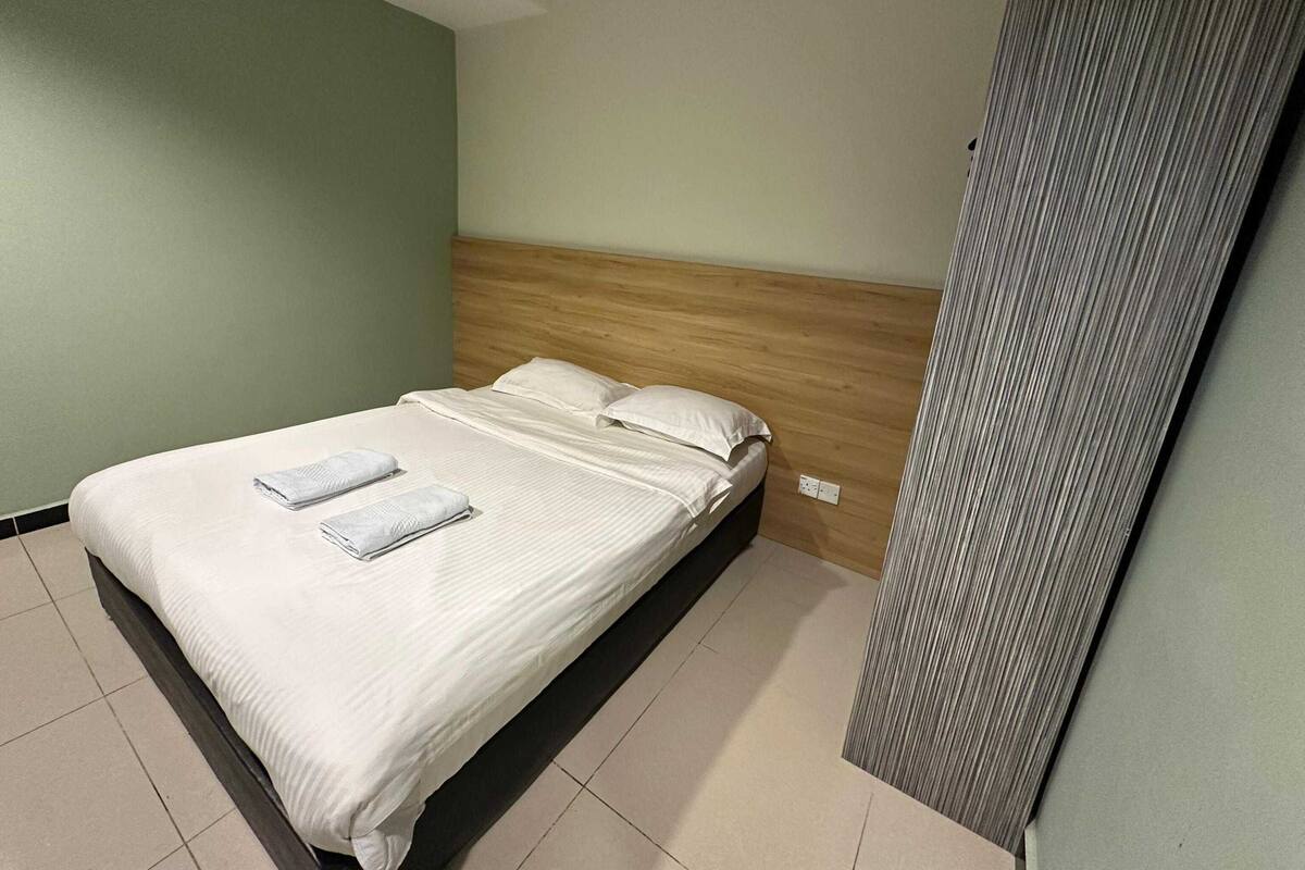 Una cama bien tendida con sábanas y almohadas blancas, un cabecero de madera y un piso de baldosas.