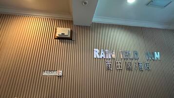 A hotel interior with a ribbed wall, a reception desk, and a sign reading "RAIN LEED INN".