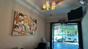 En reception med et blomsterbillede, en lysekrone, et fjernsyn og udsigt til en parkeret bil.