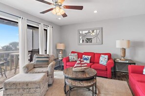 A living room with a red sofa, a wooden coffee table, a patterned armchair, and a ceiling fan. - Private beach access, Gulf Views, on-site golf car (Santa Rosa Beach)