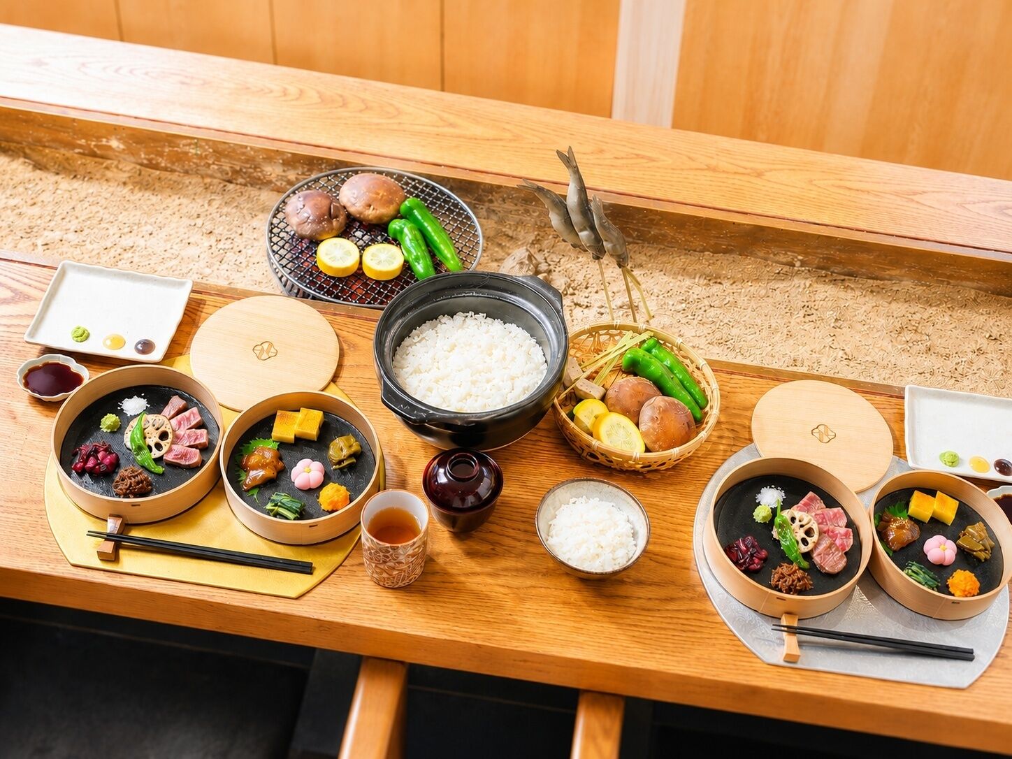 A traditional Japanese meal setup with various dishes, including rice, meat, and vegetables, arranged on a wooden table.