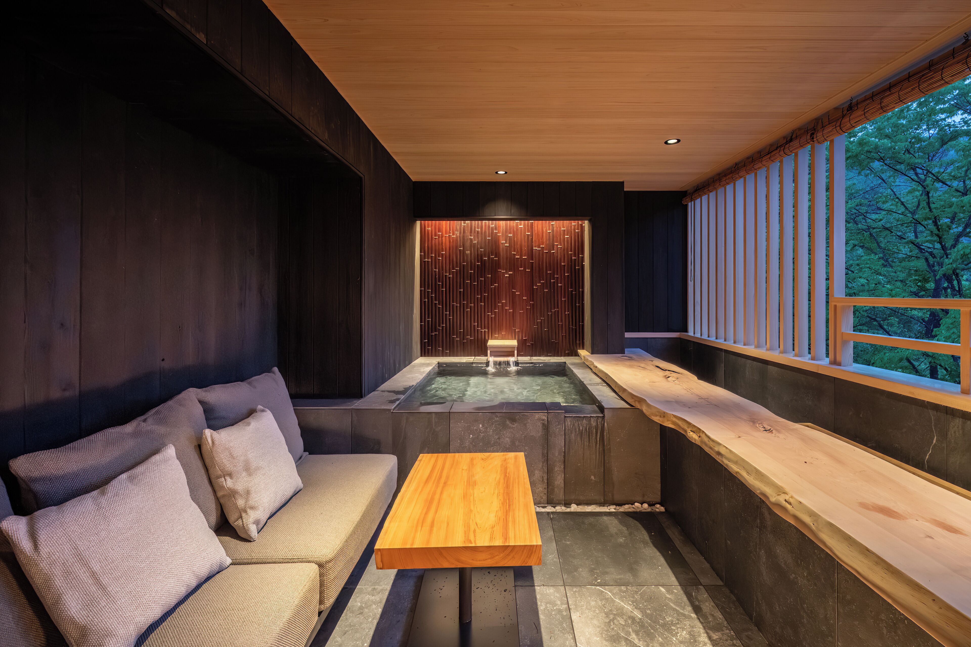 A modern interior with a wooden bench, a cushioned sofa, and a small pool area.