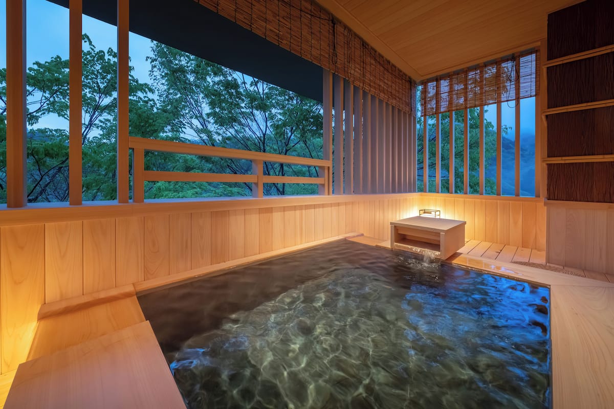 A wooden spa area with a hot tub, wooden walls, and a view of trees through large windows.