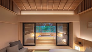 A modern hotel room with a large bed, a sofa, and a sliding glass door leading to a private outdoor area with a hot tub. - Nazuna Hakone Miyanoshita (Hakone)