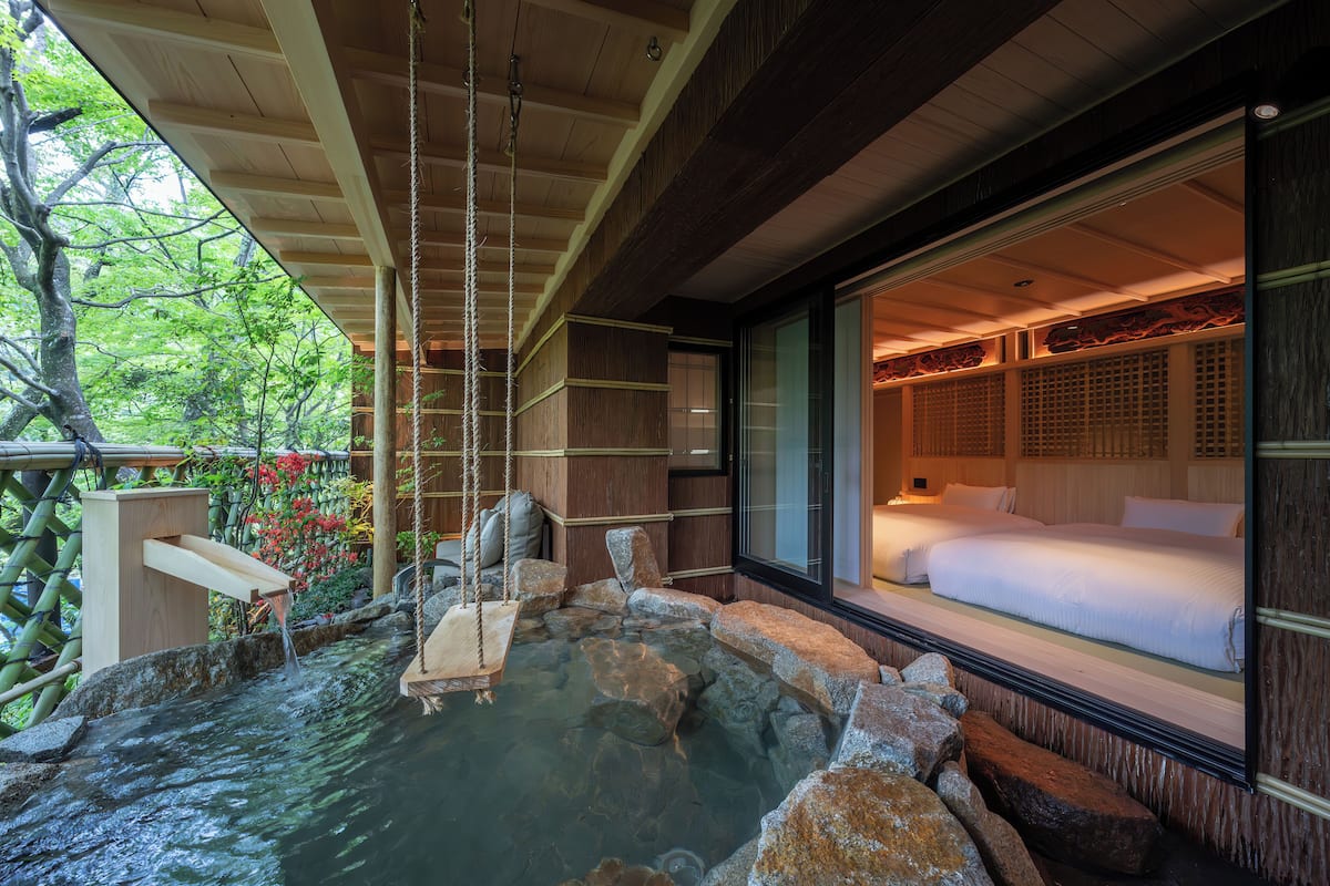 A traditional Japanese-style room with a private outdoor hot spring, wooden architecture, and a bed with white bedding.