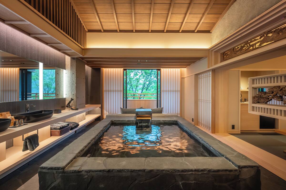 A modern bathroom with a stone sink, wooden shelves, and a view of greenery outside.