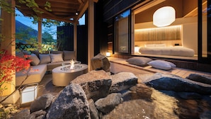 A modern outdoor seating area with a fire feature, a water stream, and a view of a well-lit interior room. - Nazuna Hakone Miyanoshita (Hakone)