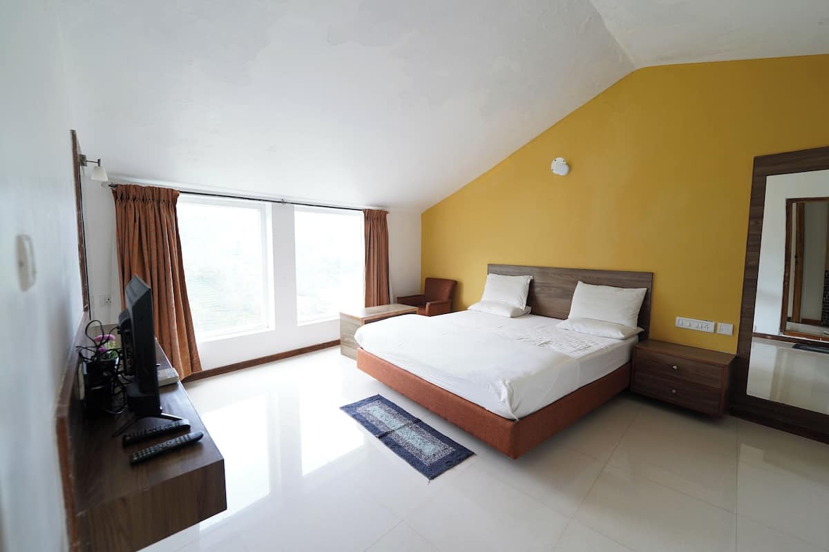 A modern hotel room with a large bed, a desk with a computer, and a window with curtains.
