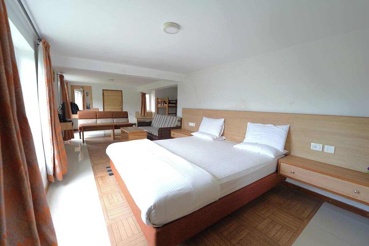 A spacious hotel room with a large bed, wooden flooring, a desk, and a chair.