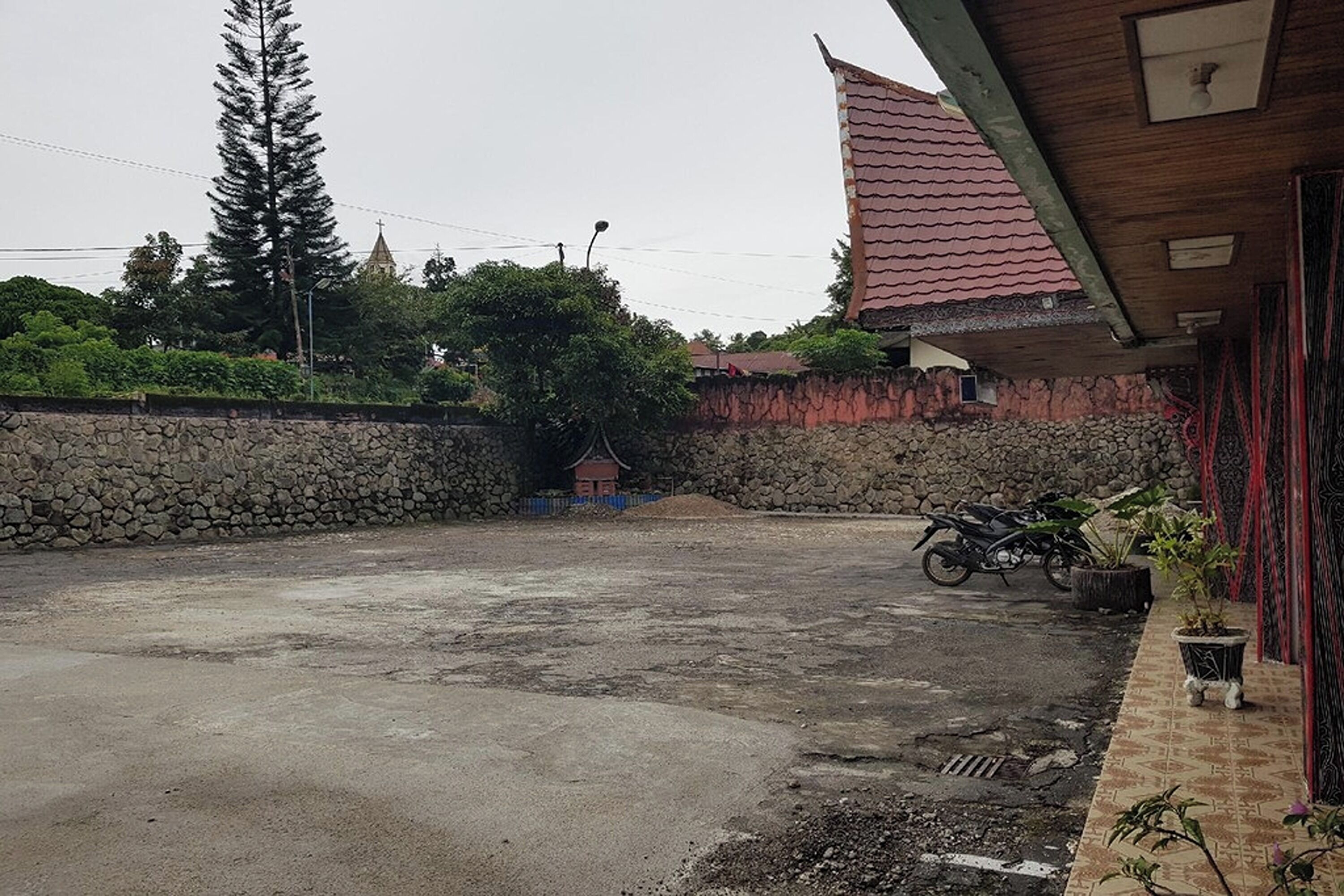 A courtyard with a stone wall, a motorcycle, and a small building with a red roof.