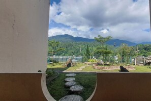 A view of a landscaped garden with a stone pathway, a fenced area, and a mountain in the background. - Hermina Hotel (Parapat)