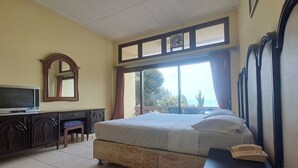 Una camera d'albergo con un letto, una scrivania con televisore, telefono e una finestra con tende.