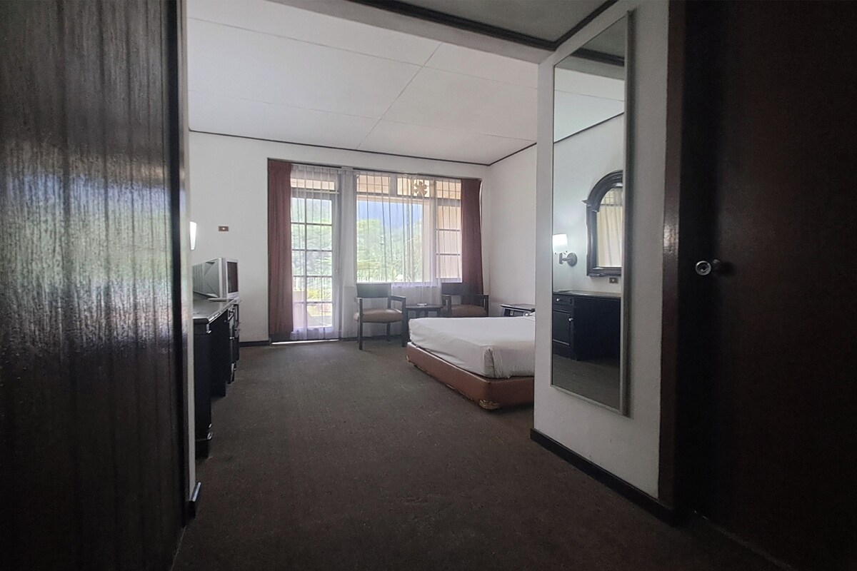 A hotel room with a bed, a desk with a computer, a chair, and a window with curtains.