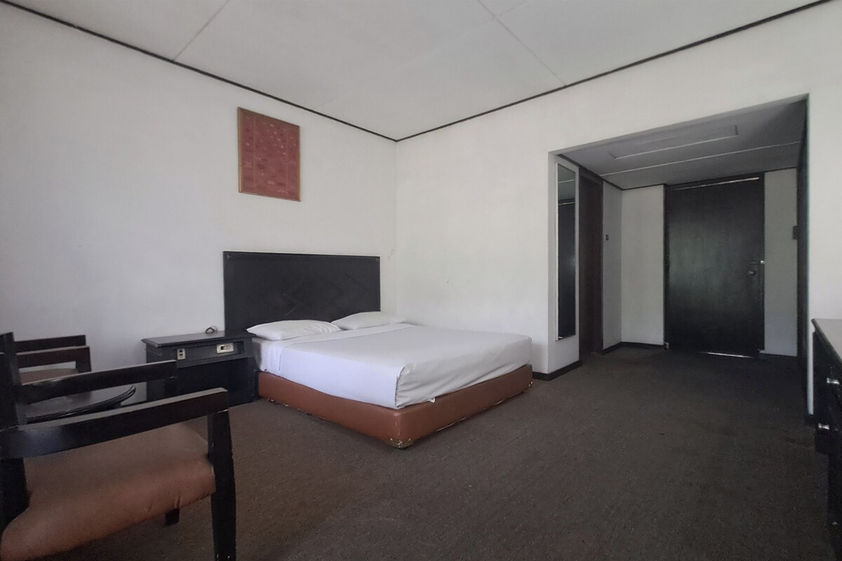 A hotel room with a single bed, a desk with a chair, and a door leading to another room.