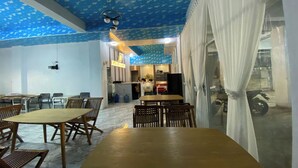 A dining area with wooden tables and chairs, a kitchen in the background, and a blue patterned ceiling. - Ranls Dream Syari'Ah Banda Aceh (Banda Aceh)