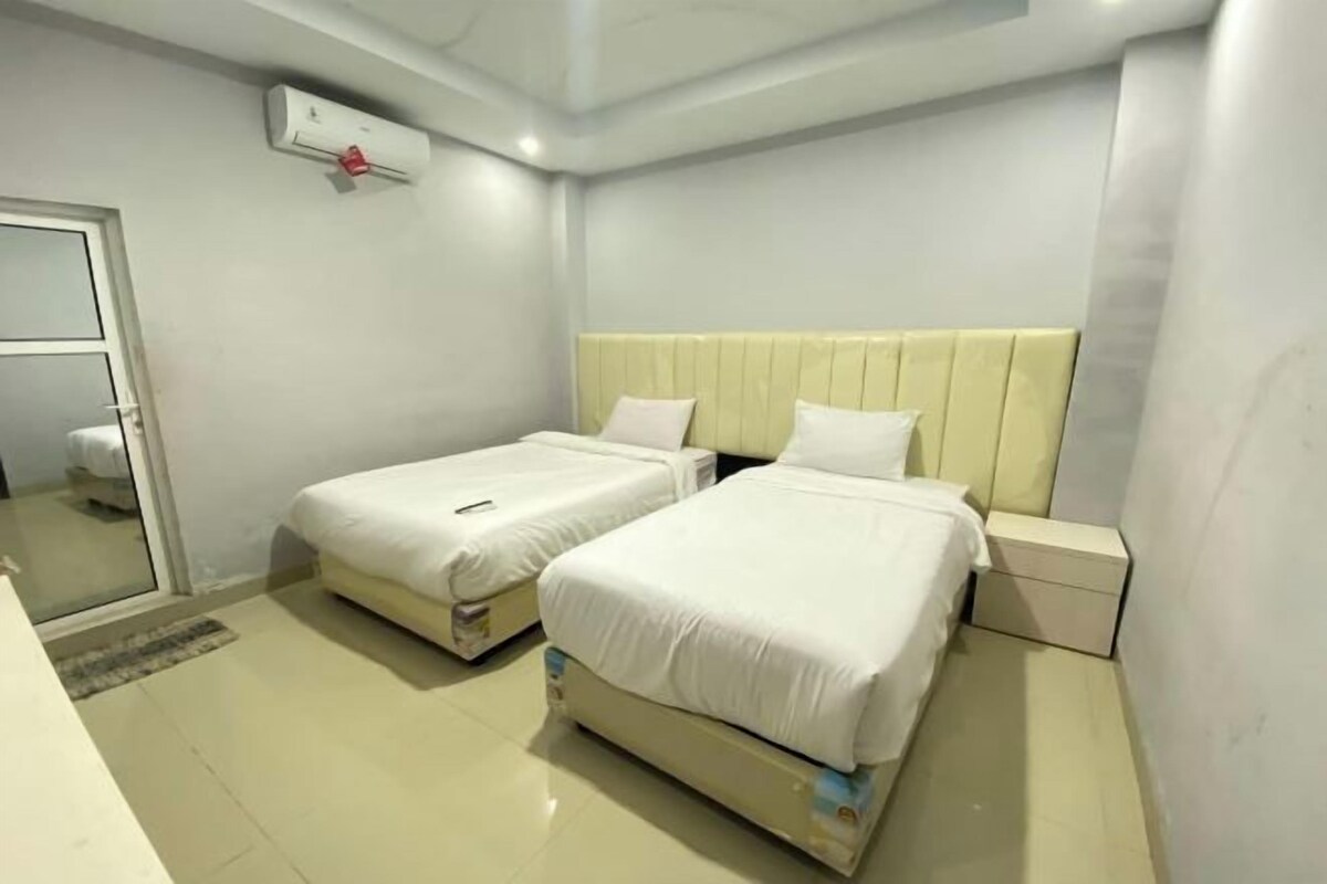 A hotel room with two beds, a bedside table, a nightstand, a mirror, and an air conditioning unit.