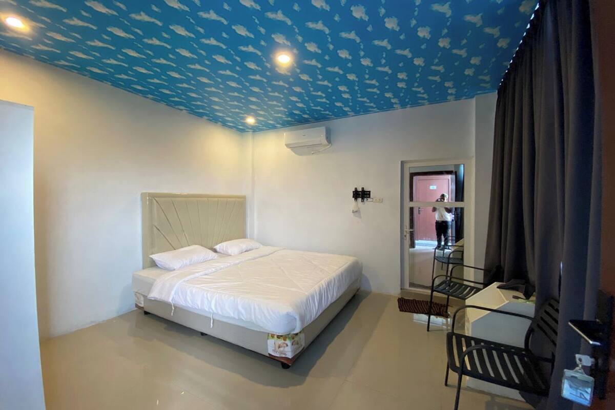 A bedroom with a bed, a chair, a mirror, and a ceiling with a cloud pattern.
