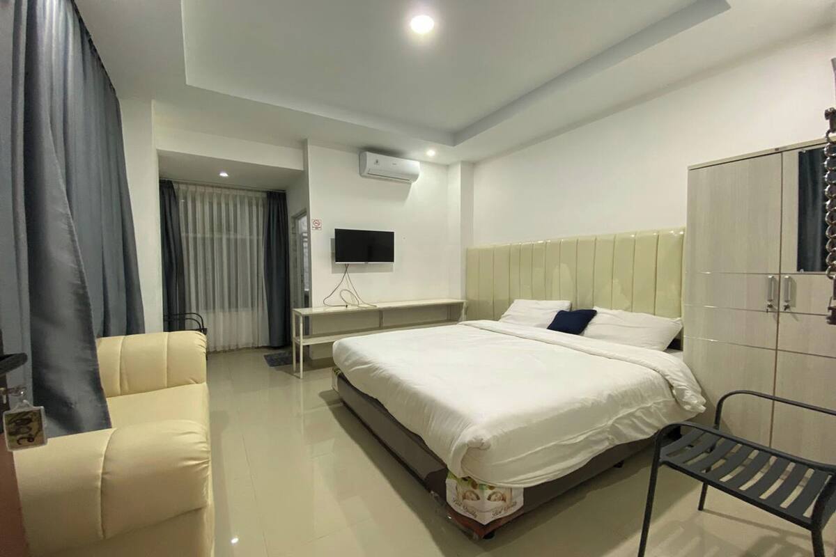 A modern hotel room with a large bed, a bedside table, a TV, and a wardrobe.