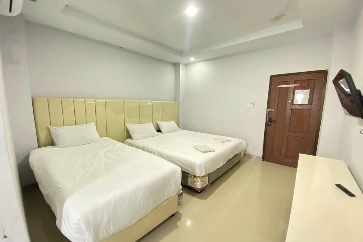A hotel room with two beds, a wooden door, a TV mounted on the wall, and a small desk.