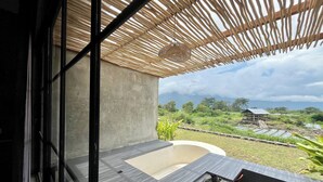 Ein moderner Außenbereich mit Betonstruktur, einem Holzdach aus Latten und Blick auf eine üppige Landschaft mit Gebäuden in der Ferne.