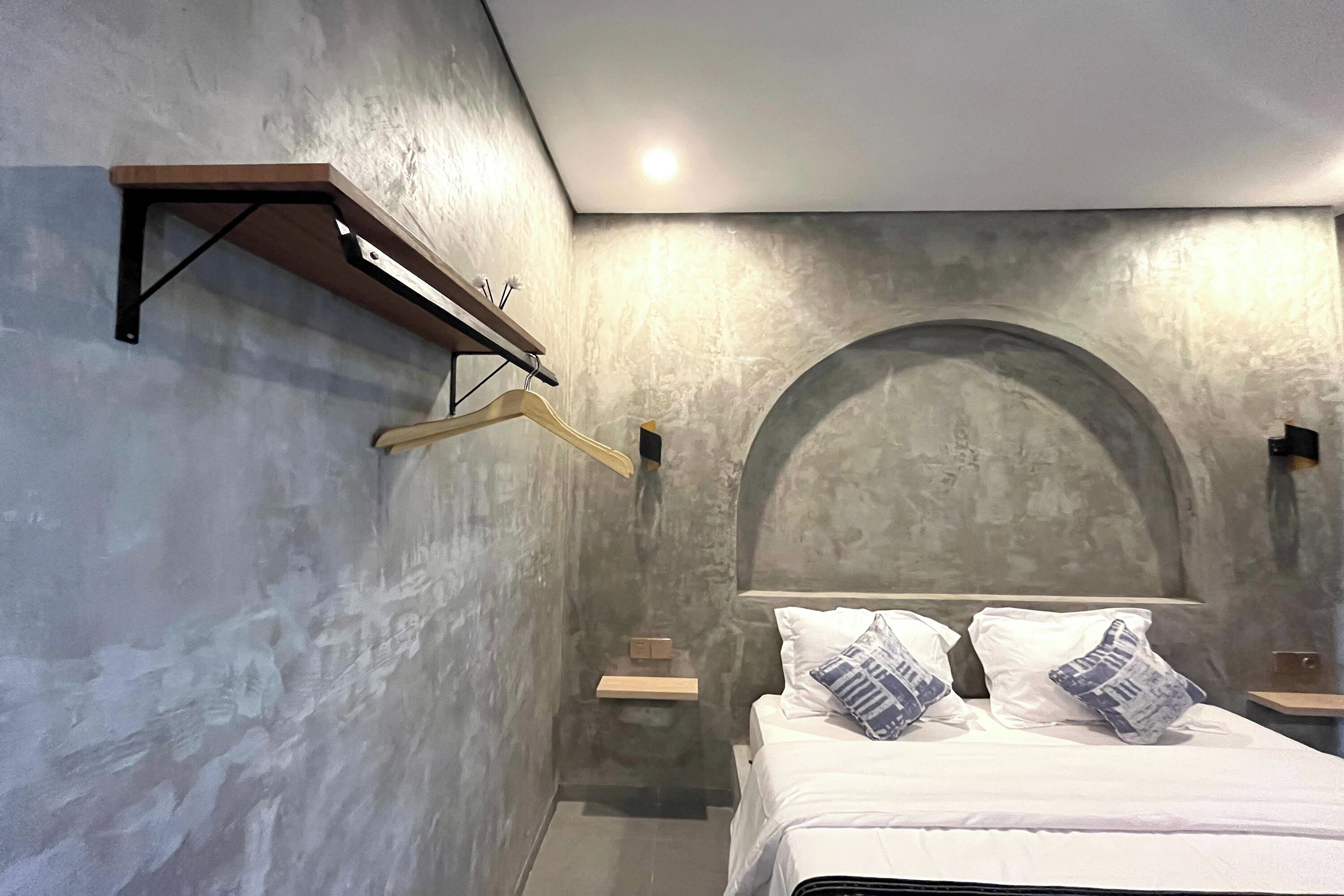 A bedroom with a bed, a wooden shelf, and a wall-mounted light fixture.