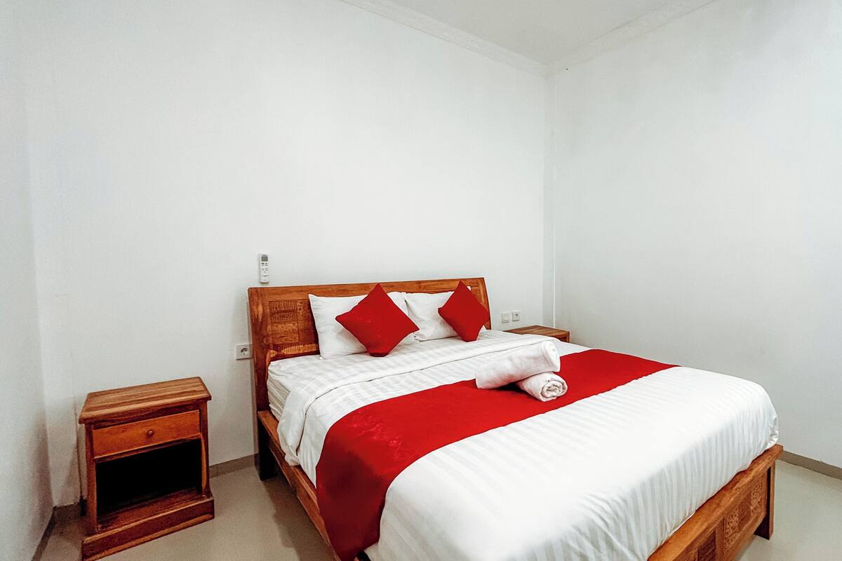 Cama bem arrumada com cabeceira de madeira, edredom vermelho e branco e duas almofadas vermelhas.