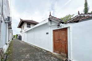 A narrow alleyway with a white building on the right, a wooden door labeled "Villa Roxo," and a traditional tiled roof. - Villa Rocko (Seminyak)