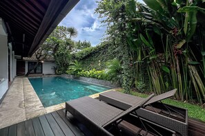 A swimming pool with lounge chairs, surrounded by lush greenery and a wooden deck. - Villa Rocko (Seminyak)