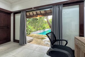 A room with a view of a swimming pool, a chair, and a wooden cabinet. - Villa Rocko (Seminyak)