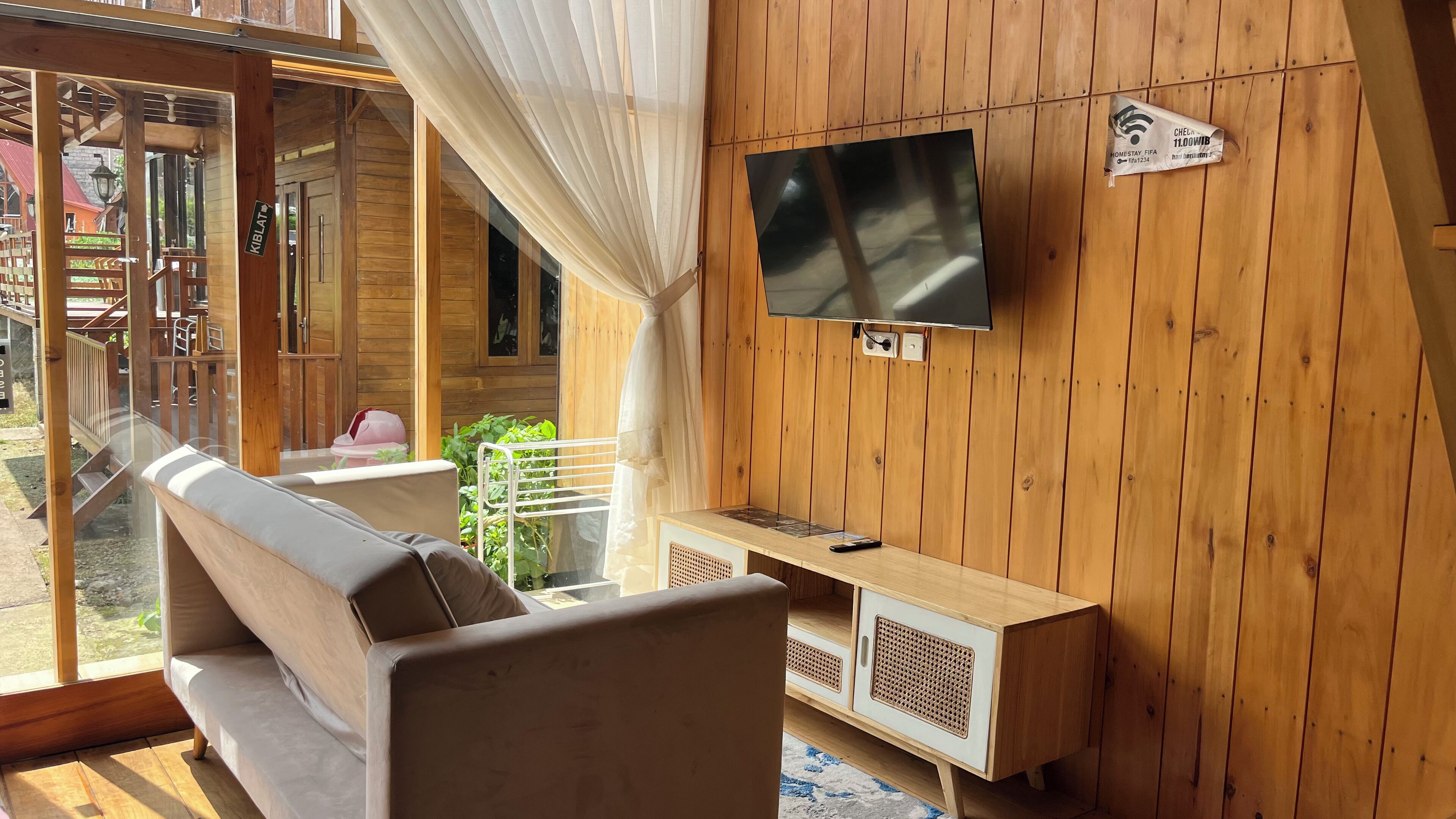 A cozy room with a wooden wall, a flat-screen TV mounted above a wooden cabinet, and a cushioned bench.