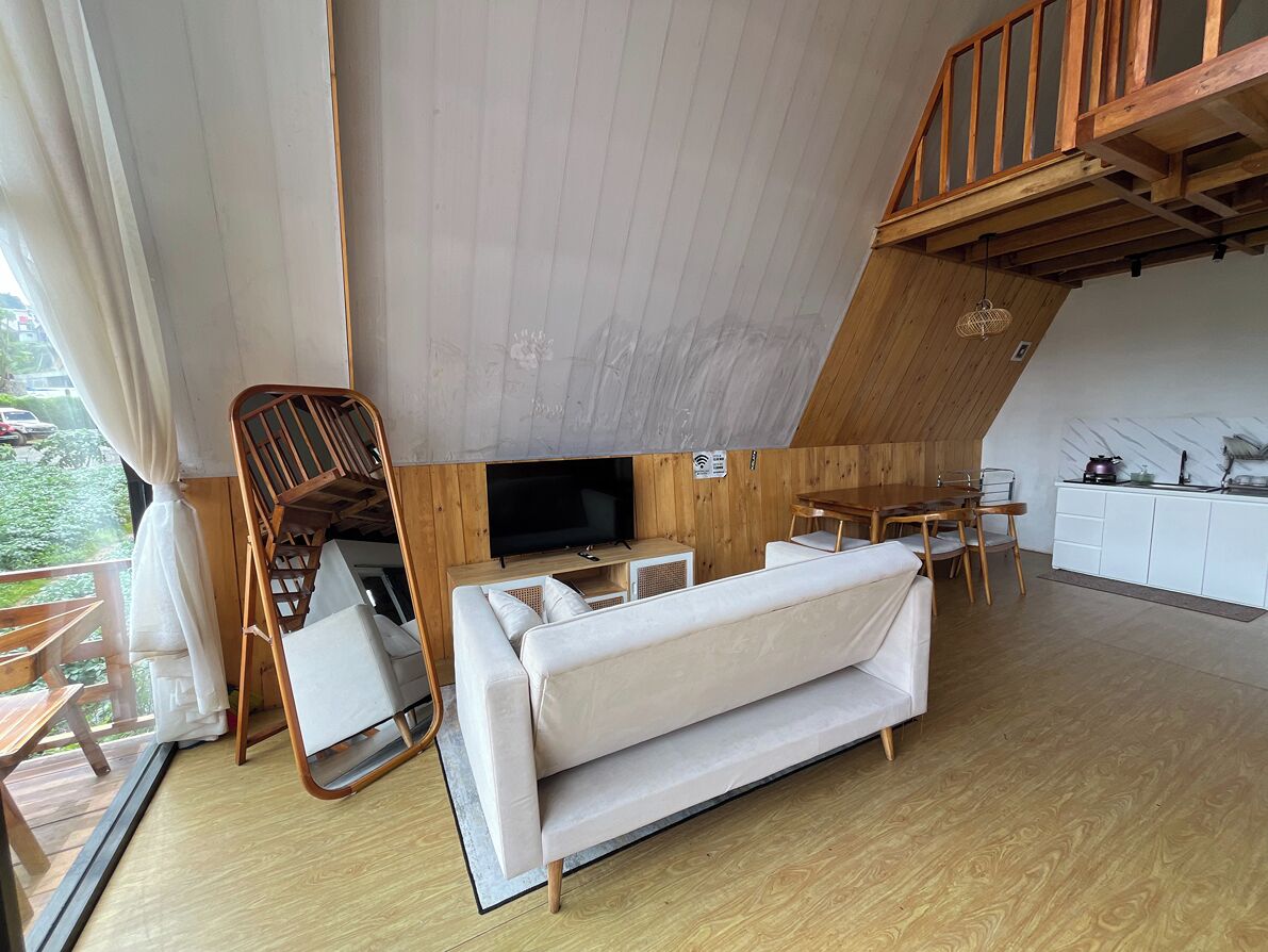 A modern living room with a sofa, TV, wooden dining table, and kitchen area.
