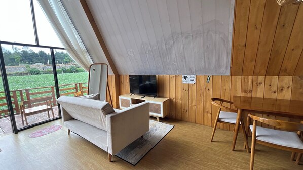 A modern living room with a sofa, TV, wooden cabinet, and a dining table with chairs.