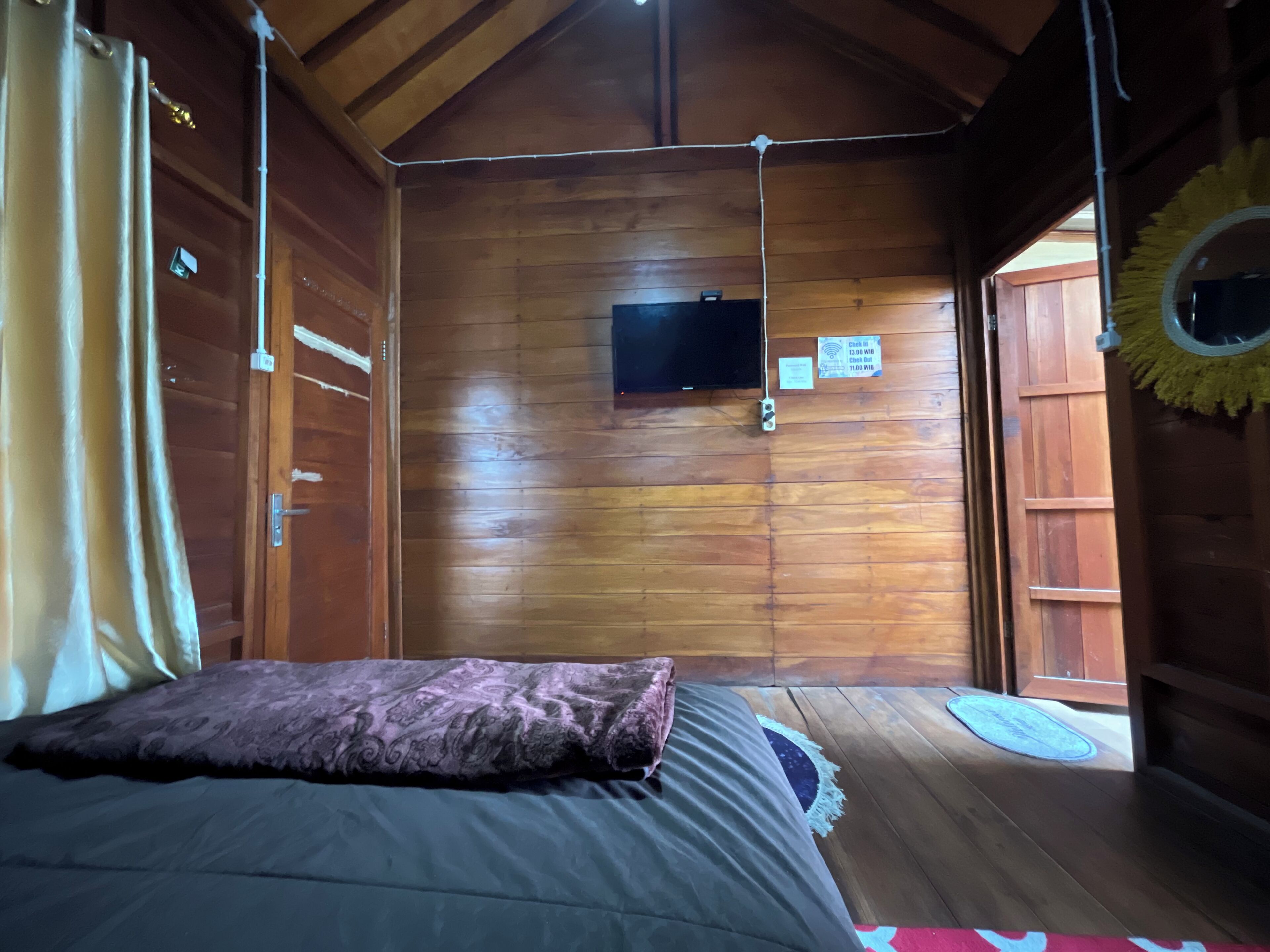 A wooden cabin room with a bed, a mounted television, and a door leading outside.