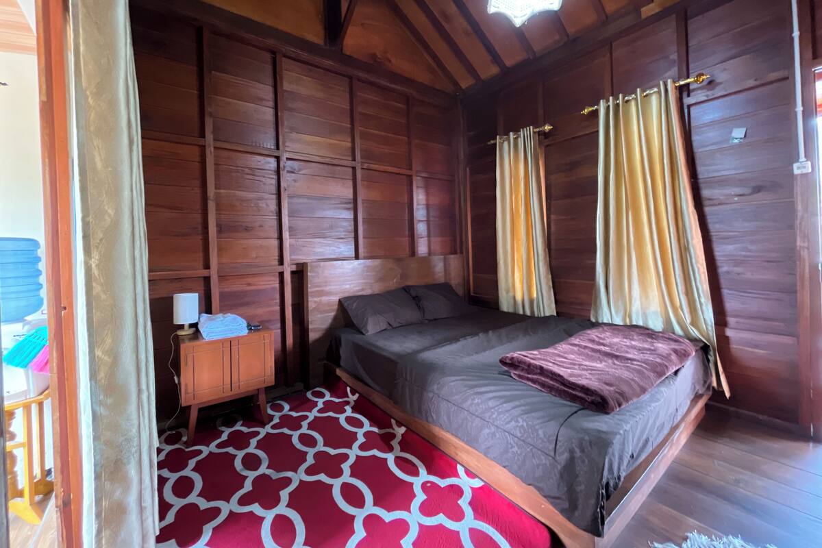 A wooden room with a bed, curtains, and a nightstand.