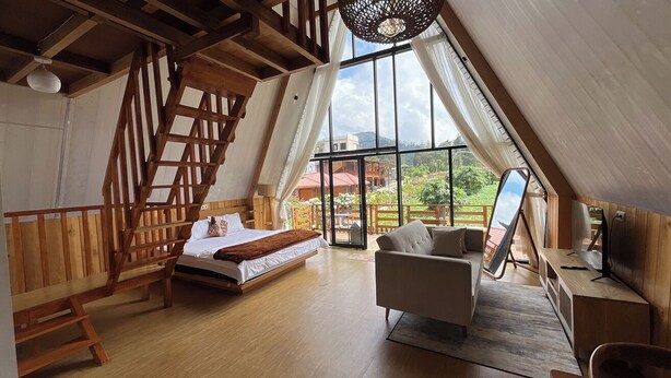 A spacious room with a wooden staircase, a bed, a sofa, and a large window offering a view of the outdoors. - Fifa Cabin Dieng By Fifa Grup (Dieng Kulon)