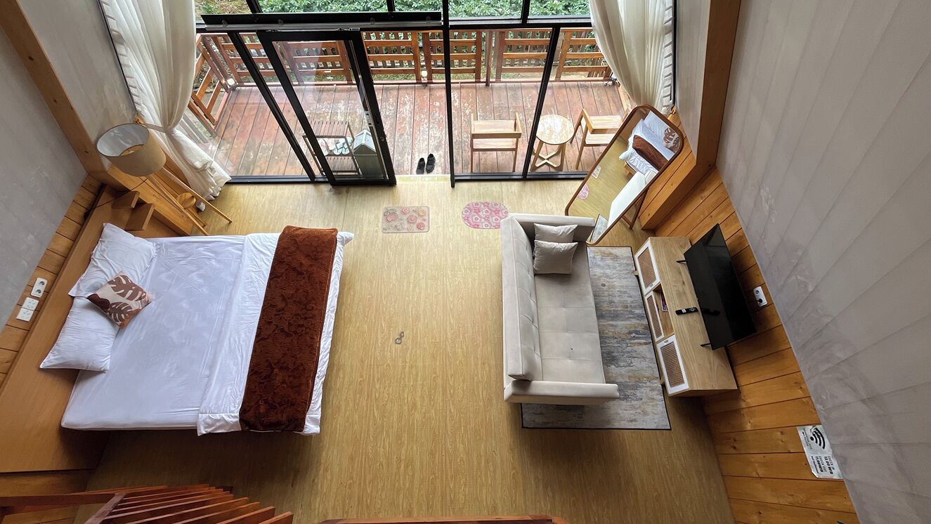 A bedroom with a bed, a sofa, a TV, and a wooden floor.
