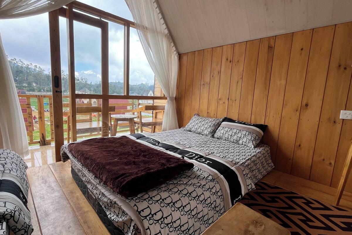 A bedroom with a bed, a wooden headboard, and a view of the outdoors through a large window.