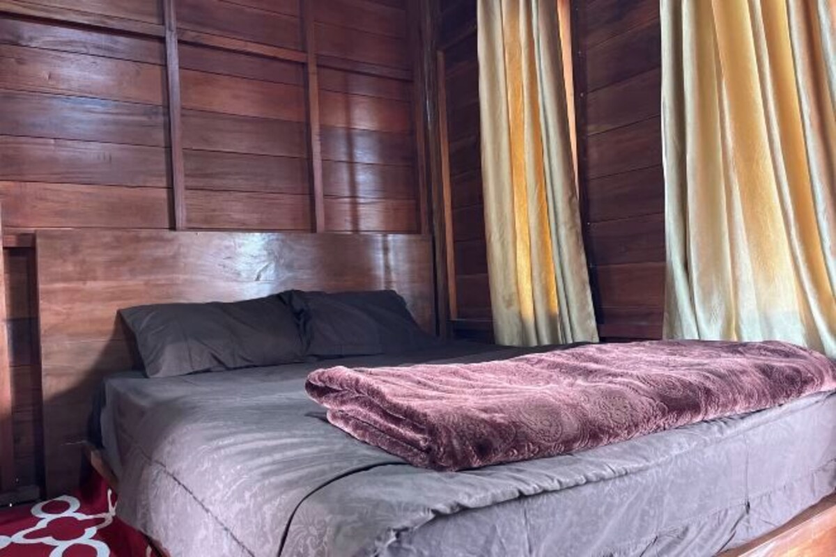 A wooden-paneled room with a bed, a headboard, and curtains.