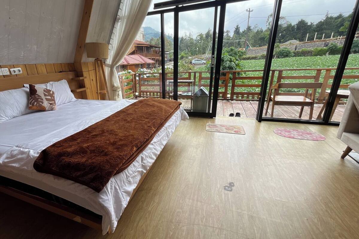 A bedroom with a large bed, wooden headboard, and a view of a garden through a sliding glass door.